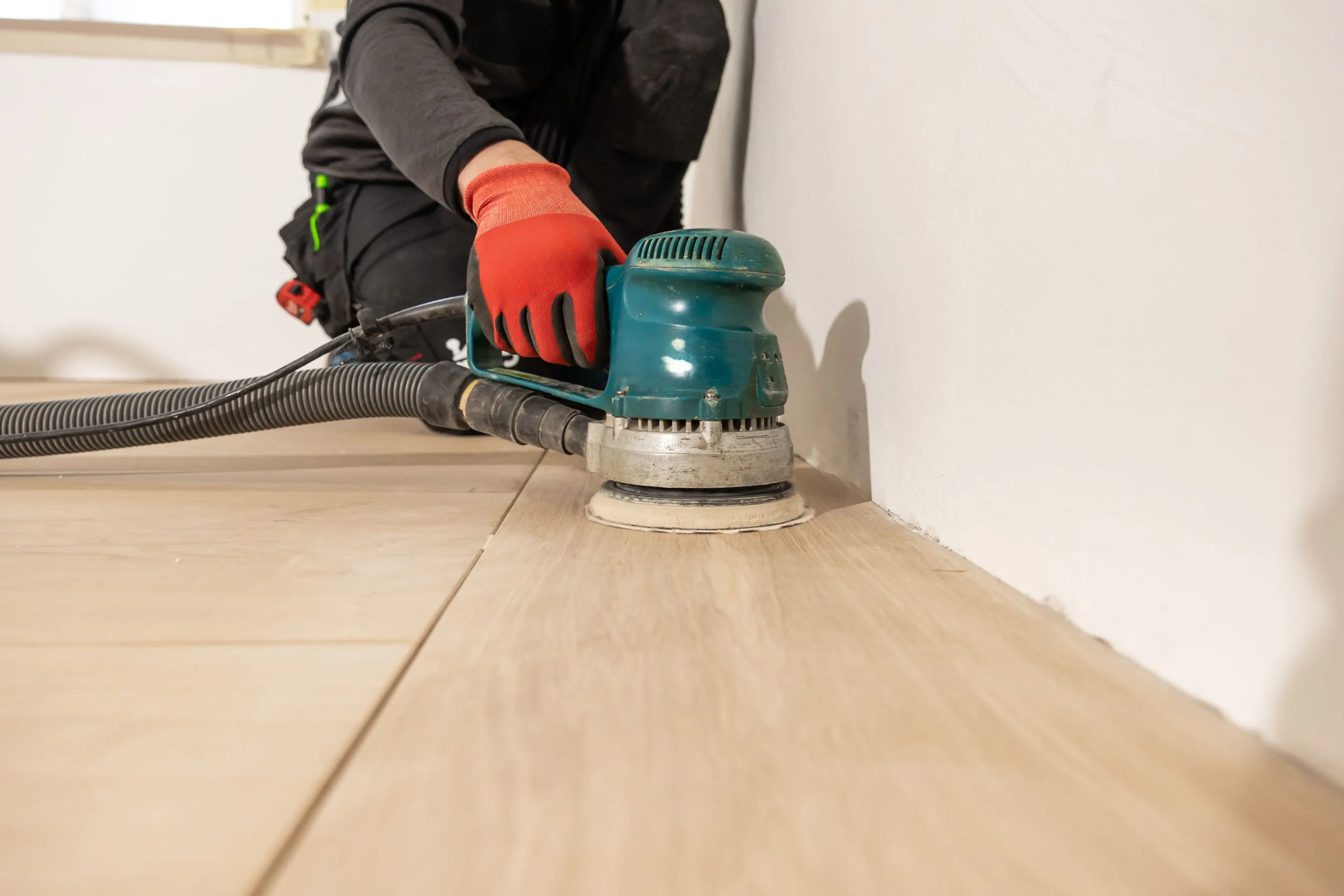 Person sanding wooden floor with electric sander.